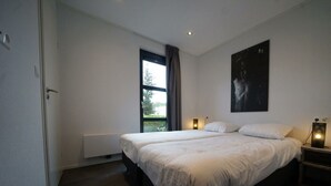Une chambre moderne avec un grand lit, une fenêtre avec des rideaux, une œuvre d’art accrochée au mur et des lampes de chevet.