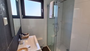 Une salle de bain moderne avec une douche à l’italienne en verre, un lavabo avec un plateau en bois et une fenêtre au-dessus du miroir.