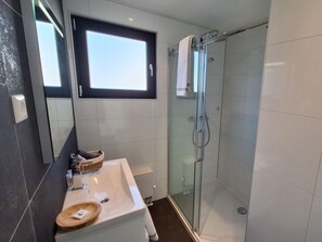 Ein modernes Badezimmer mit Duschkabine aus Glas, einem Waschbecken mit Holztablett und einem Fenster über dem Spiegel.