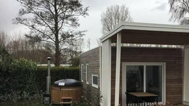 Een modern huis met een houten gevel, een terras met een tafel en stoelen, en een jacuzzi.