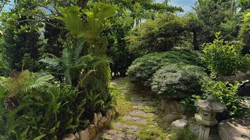 Un jardín con un camino de piedra, abundante vegetación y un farol de piedra.