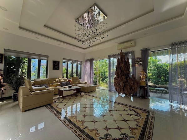 A spacious living room with a large sofa set, a decorative chandelier, and a view of greenery outside. - Bao Ong Thien Retreat (Thai My Commune)