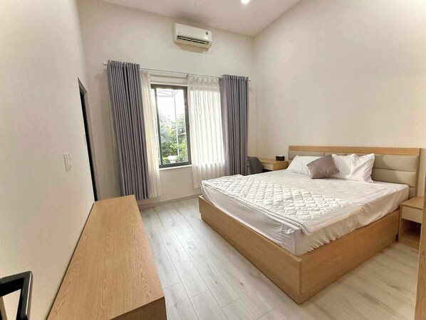 A bedroom with a bed, a desk, a chair, a window with curtains, and an air conditioning unit.