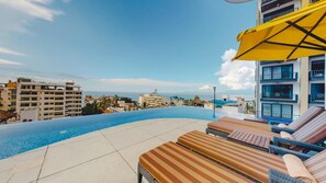 A poolside area with lounge chairs and a yellow umbrella, overlooking a body of water and buildings. - Elegant 2BR Condo with Ocean View Balcony! 2BD Condo for rent in Amapas, Puerto (Puerto vallarta)