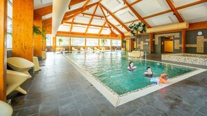 Une piscine intérieure dotée d’un haut plafond, de poutres en bois et de chaises longues.