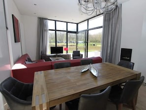 A modern dining area with a wooden table, red seating, and large windows offering a view of a lake. - Holiday Home in Otterlo With Terrace (Otterlo)