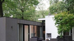 Un espace de vie extérieur moderne, doté d’une cheminée intégrée, de sièges et d’une grande fenêtre donnant sur un jardin.
