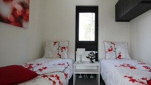 Une chambre avec deux lits, une petite table et une fenêtre.