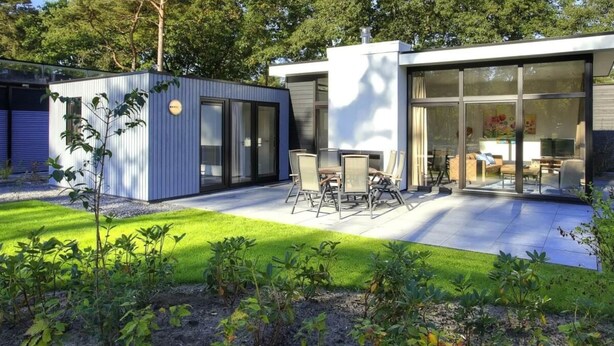 Une maison moderne dotée d’un patio, d’un petit jardin et d’un coin repas aménagé avec du mobilier d’extérieur.