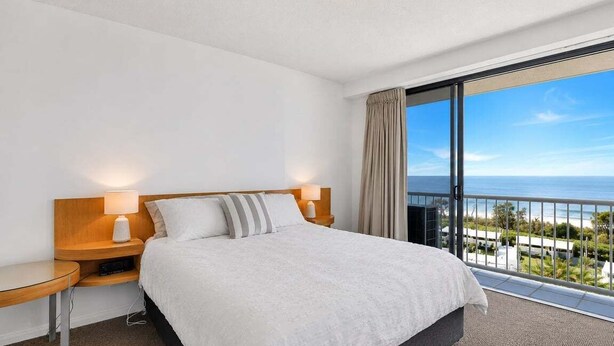 Une chambre d’hôtel avec un lit, des tables de chevet, une vue sur l’océan et un balcon.