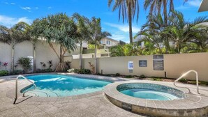 Une piscine entourée d’une terrasse, avec des palmiers et un bâtiment en arrière-plan.