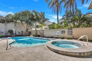 A swimming pool with a surrounding deck, palm trees, and a building in the background. - Amazing Ocean Views from Unit 87-Catalina-II (Maroochydore)
