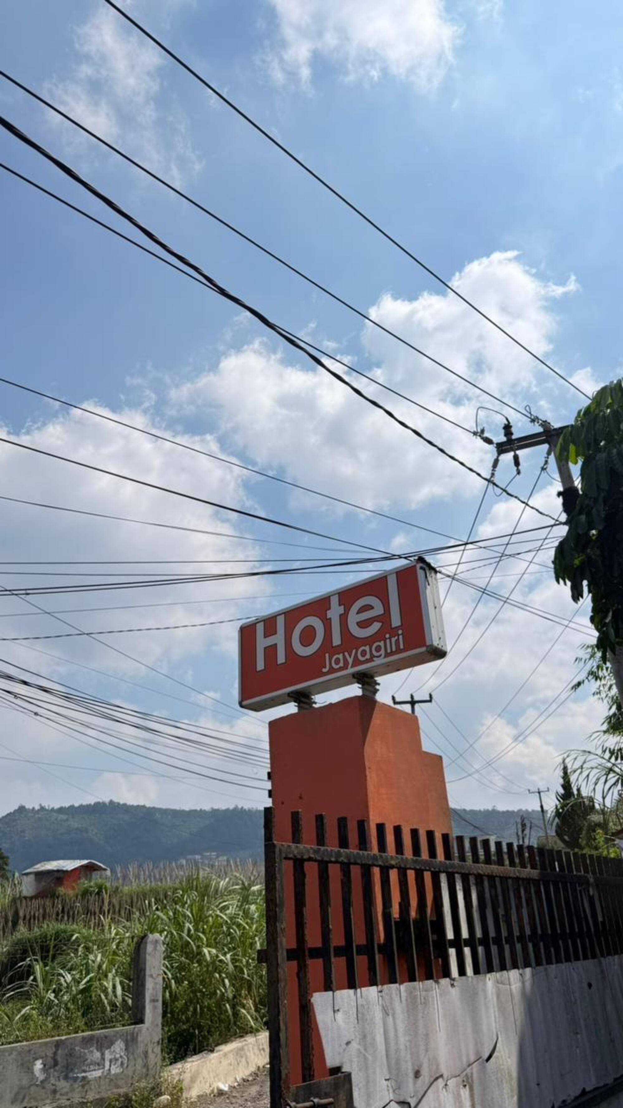 A sign for a hotel named 'Hotel Layagiri' with a fence and power lines in the background.