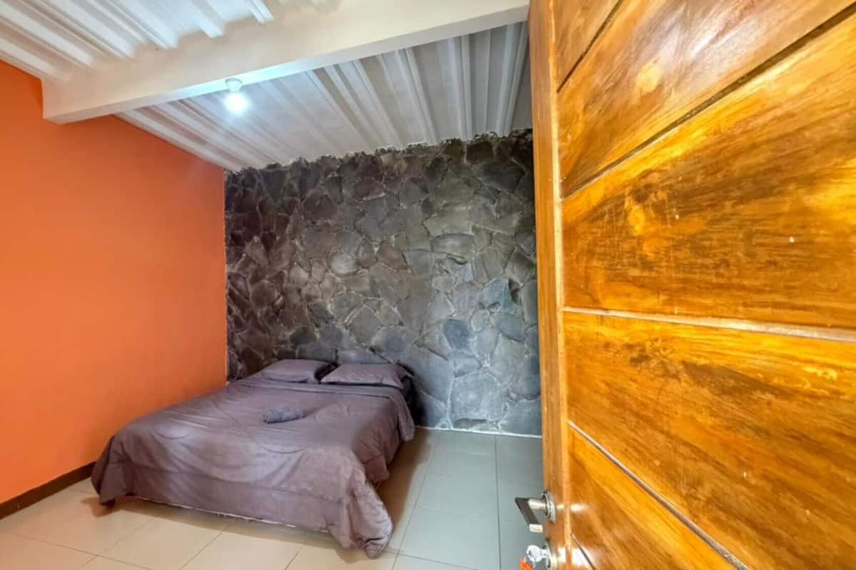 A room with a bed, a stone wall, an orange wall, and a wooden door.