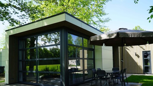 A modern outdoor patio with a glass enclosure, a table with chairs, and an umbrella. - Holiday Home in Kaatsheuvel With Terrace (Kaatsheuvel)