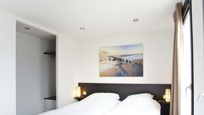 A hotel room with a bed, two bedside tables with lamps, a painting on the wall, and a door leading to another room. - Holiday Home in Kaatsheuvel With Terrace (Kaatsheuvel)
