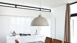 A modern kitchen with white cabinets, a central island, a dining table with chairs, and a pendant light. - Holiday Home in Kaatsheuvel With Terrace (Kaatsheuvel)