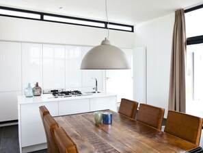 A modern kitchen with white cabinets, a central island, a dining table with chairs, and a pendant light. - Holiday Home in Kaatsheuvel With Terrace (Kaatsheuvel)
