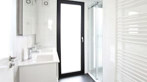 A modern bathroom with a large mirror, a white sink, and a glass shower enclosure. - Holiday Home in Kaatsheuvel With Terrace (Kaatsheuvel)