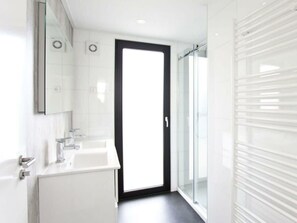 A modern bathroom with a large mirror, a white sink, and a glass shower enclosure. - Holiday Home in Kaatsheuvel With Terrace (Kaatsheuvel)