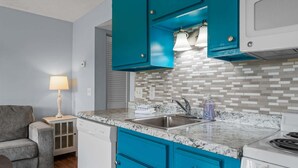Une cuisine compacte avec des meubles de couleur turquoise, un plan de travail en granit, une cuisinière encastrée et un évier.