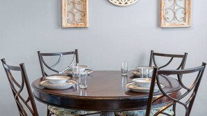 Une table de salle à manger ronde, accompagnée de six chaises, chacune ornée d’un coussin à motifs floraux.