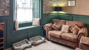 Une pièce avec un mur recouvert de lambris verts, un canapé marron, un banc de fenêtre, une lampe et une carte encadrée.
