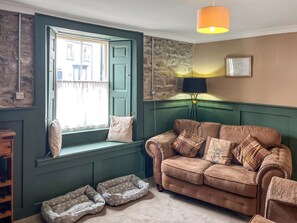 Ein Zimmer mit grüner Wandverkleidung, einem braunen Sofa, einer Sitzbank an einem Fenster, einer Lampe und einer gerahmten Karte.