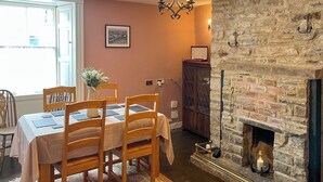 Une salle à manger avec une table dressée pour quatre personnes, une cheminée et un mur en pierre.