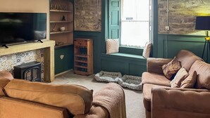 Un salon chaleureux avec une cheminée, un téléviseur, un canapé et un coin lecture près de la fenêtre.