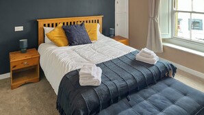 Une chambre à coucher avec un lit, des tables de chevet, un banc, une fenêtre et une porte.