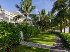 Un camino bordeado de palmeras que conduce a un edificio de fachada blanca y balcones.