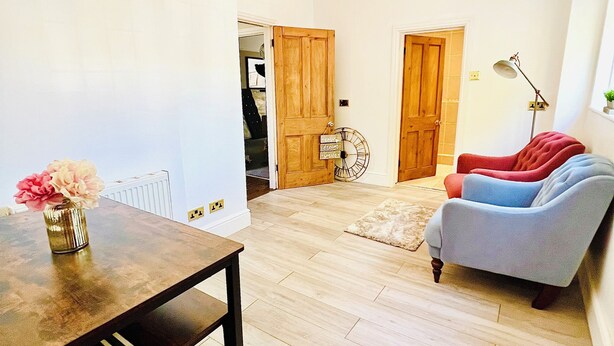Una habitación con una mesa de comedor de madera, un sofá, un radiador y una puerta que da a otra habitación.
