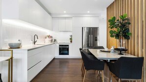 A modern kitchen with white cabinets, a stainless steel refrigerator, and a dining area with a table and chairs. - Elegant Remuera 2BDR Retreat Prime Location (Auckland)