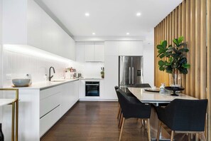 Una cocina moderna con armarios blancos, un refrigerador de acero inoxidable y una zona de comedor con una mesa y sillas.