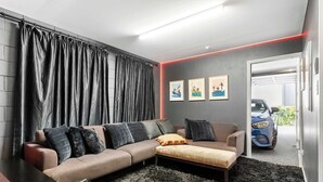 A modern living room with a sectional sofa, a coffee table, and a black furry rug. There are three framed artworks on the wall and a car visible through an open door. - Elegant Remuera 2BDR Retreat Prime Location (Auckland)