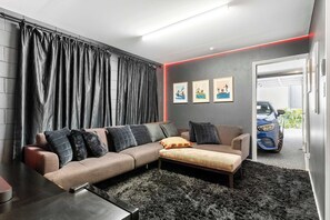 Una sala de estar moderna con un sofá modular, una mesa de centro y un tapete mullido negro. Hay tres cuadros enmarcados en la pared y se ve un coche a través de una puerta abierta.