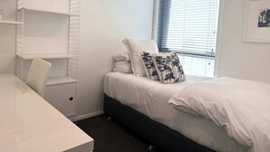 A bedroom with a bed, a desk, a chair, and a window with blinds. - Elegant Remuera 2BDR Retreat Prime Location (Auckland)