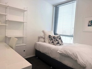 Un dormitorio con cama, escritorio, silla y ventana con persianas.
