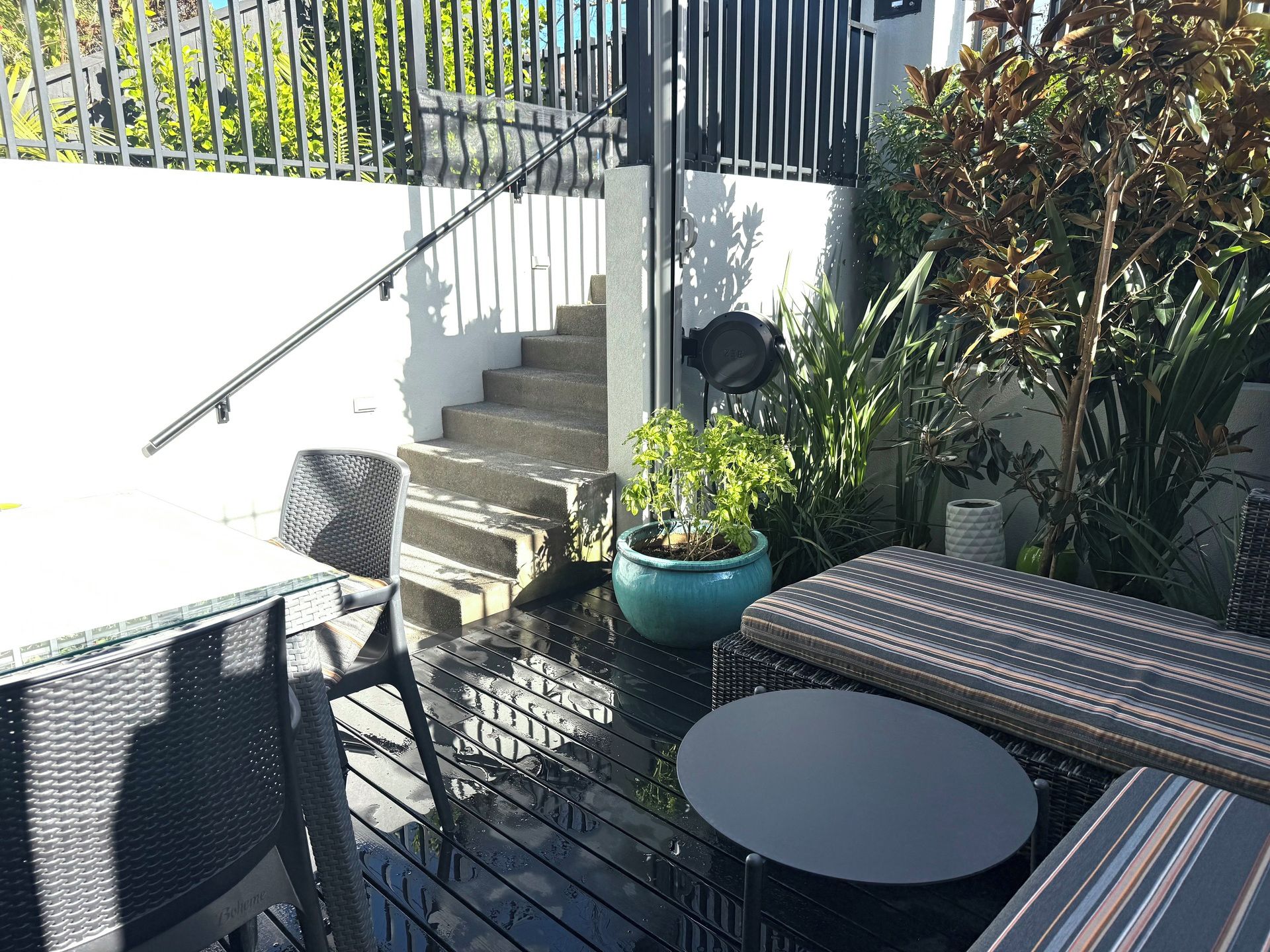 Un espace patio aménagé avec du mobilier d’extérieur, une plante en pot et un escalier menant à un niveau supérieur.