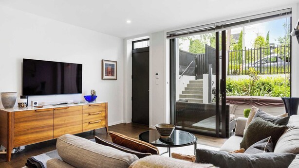 A modern living room with a flat-screen TV, wooden cabinet, and a glass table. - Elegant Remuera 2BDR Retreat Prime Location (Auckland)