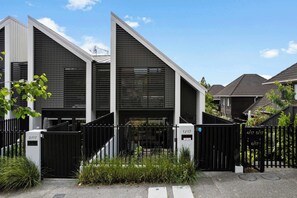 A modern building with a sloped roof, a gated entrance, and a small garden area. - Elegant Remuera 2BDR Retreat Prime Location (Auckland)