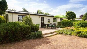 A single-story building with a gravel driveway, a patio with outdoor seating, and well-maintained greenery. - Comfort 6 Persons (Egmond aan den Hoef)