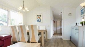 A modern dining area with a wooden table and chairs, a kitchen with cabinets, and a hallway leading to another room. - Comfort 6 Persons (Egmond aan den Hoef)