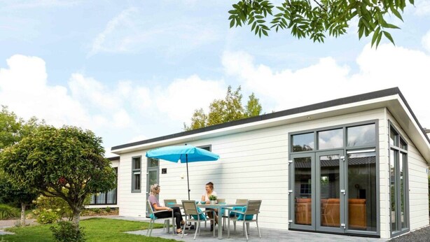 A modern house with a patio, a dining table, and two people seated. - Comfort 6 Persons (Egmond aan den Hoef)