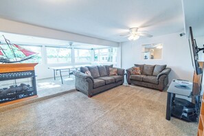 A spacious living room with two sofas, a coffee table, a ceiling fan, and a large window providing natural light.