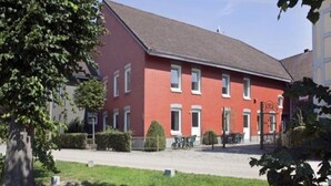 Un edificio rosso con tetto piatto, diverse finestre e un piccolo giardino antistante.