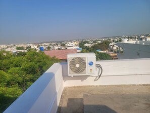 Eine Dachterrasse mit Klimaanlage, Blick auf eine Stadtlandschaft und ein wenig Grün.