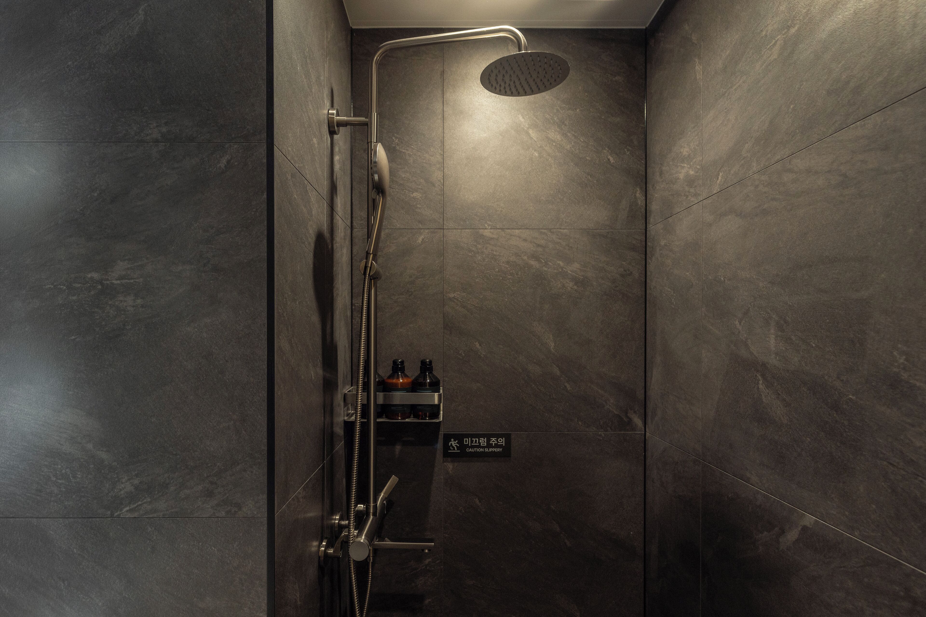 A shower with a handheld showerhead, a wall-mounted control panel, and a caution sign.