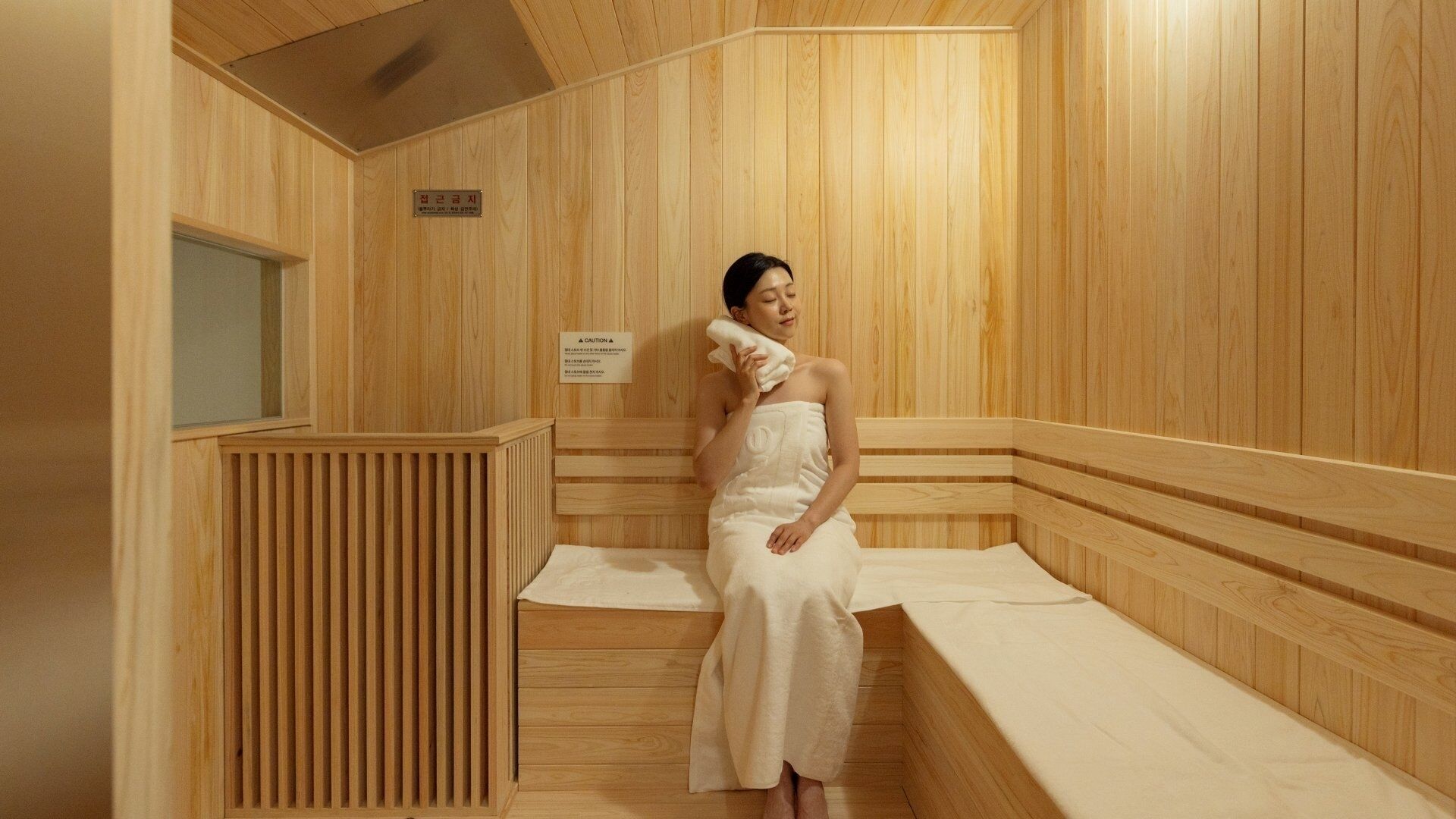 Un sauna de madera con un banco, una toalla y un letrero de precaución.